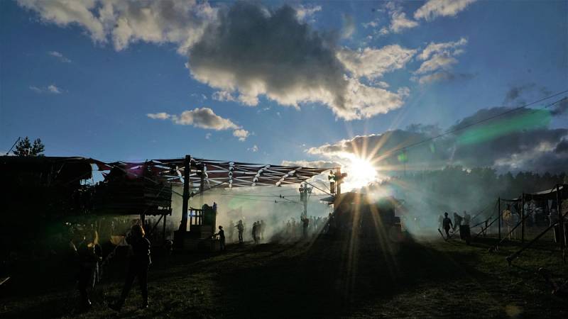 Sonnenaufgang auf dem Festival-Gelände. Nebelschwaden umhüllen tanzende Besucher vor der Sandpalast-Bühne während erste Sonnenstrahlen durch die Wolken brechen.