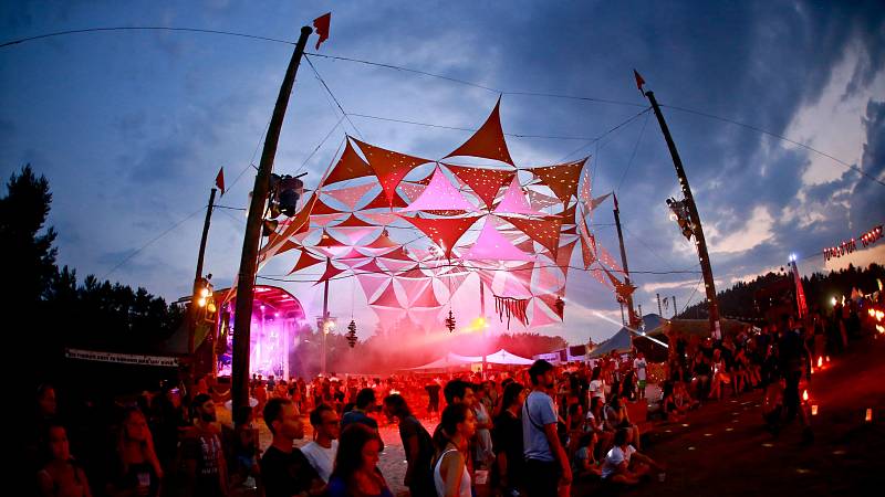 Die Sandpalast-Bühne mit ihren in bunte Farben gehüllten Sonnensegeln. Besucher und Besucherinnen schauen gebannt den Feuerkünstlern zu, welche nur teilweise im Bild zu sehen sind.