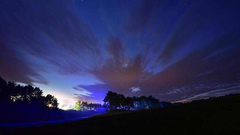 Sonnenaufgang über dem Feld der Ehre in Scherleithen. Man sieht Nebelschwaden schwer auf den Feldern liegen und sich durch Bäume schlängeln, während die ersten Sonnenstrahlen durch die Wolken brechen.