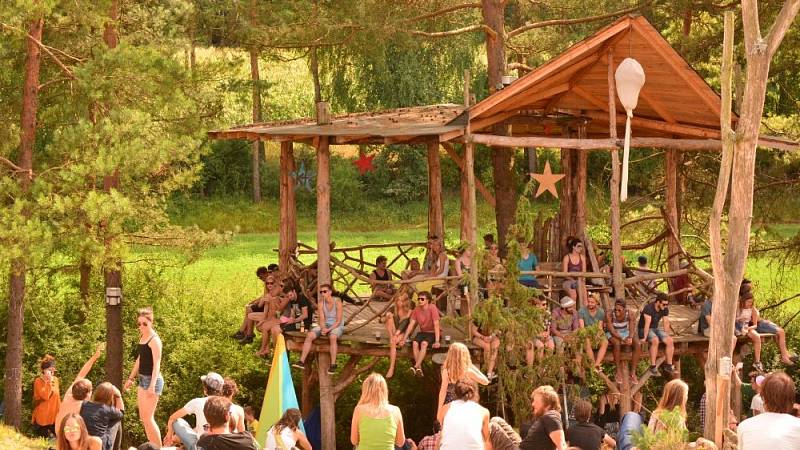 Sich in Hängematten und auf dem Baumhaus entspannende Beuscher und Besucherinnen mit ihren Familien mit Blick auf den umliegenden Wald